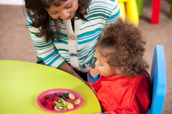 A woman helping a child eat fruit.