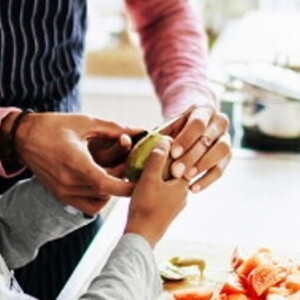 An adult helping a child to prepare fruit and vegatables