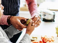 An adult helping a child to prepare fruit and vegatables