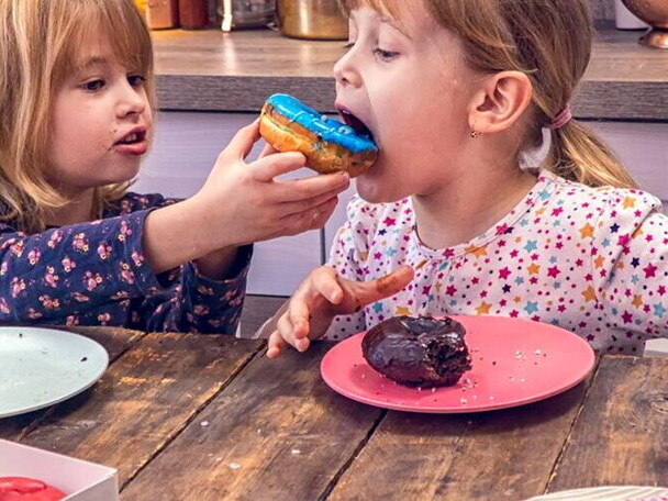 Two girls eating donuts together in the kitchen.