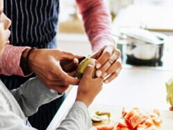 An adult helping a child to prepare fruit and vegatables