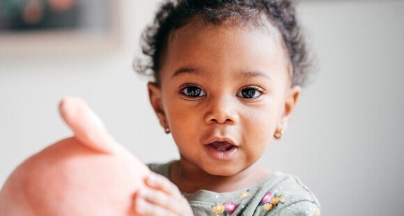 Toddler holding a large pink object indoors.