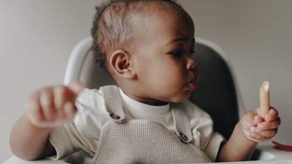 Baby in high chair holding a breadstick